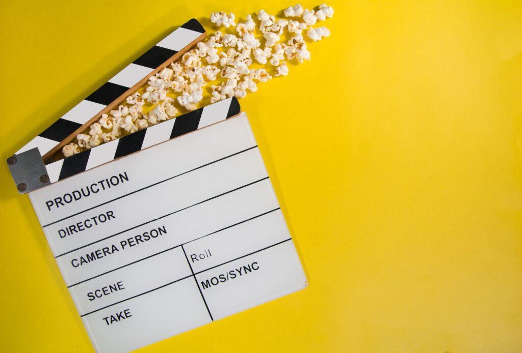 A blank movie clapperboard rests on a bright yellow background with popcorn spilled on top.