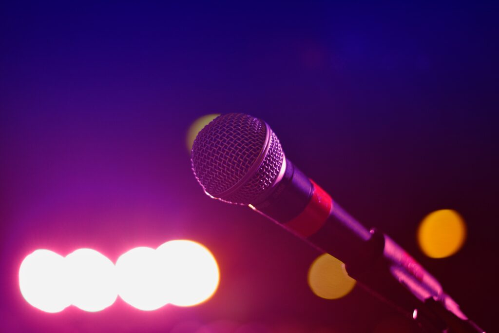 A microphone set up on stage ready for a performance, with purple lights in the distance.