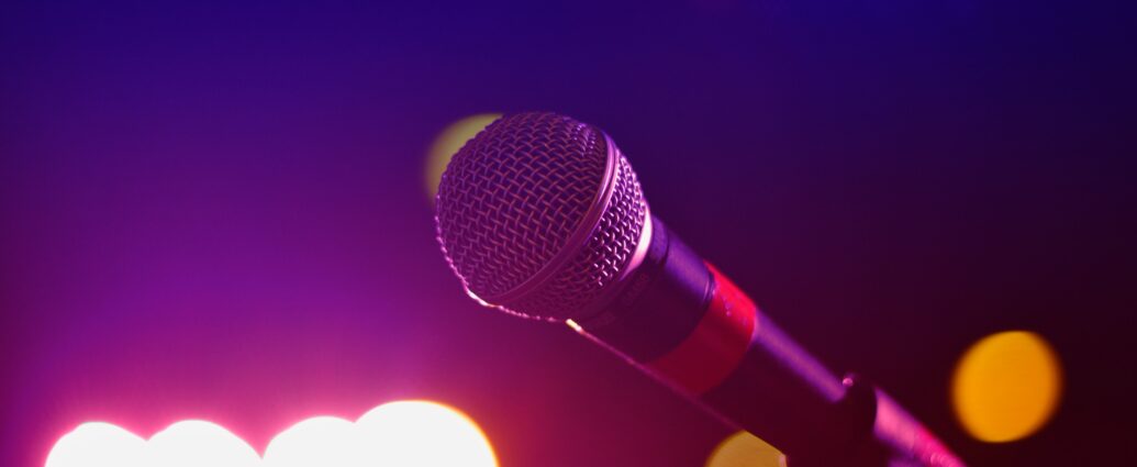 A microphone set up on stage ready for a performance, with purple lights in the distance.