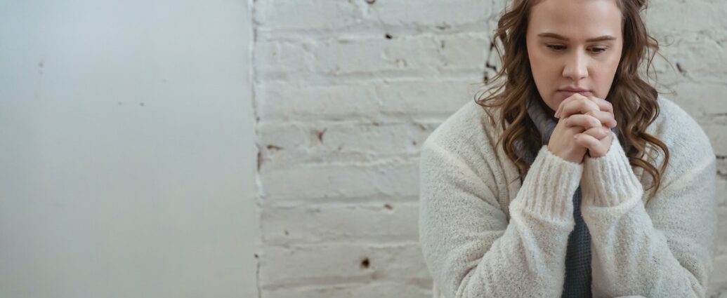 Upset woman wearing white cardigan with fingers clasped, thinking about next steps