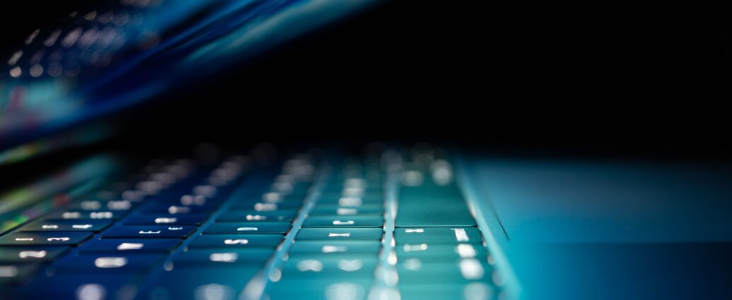 Side view of a laptop folded almost completely down. The room is dark so the only light is a blue-green glow from the screen. It sets the sinister tone of the story about Stephen Bear's crimes.