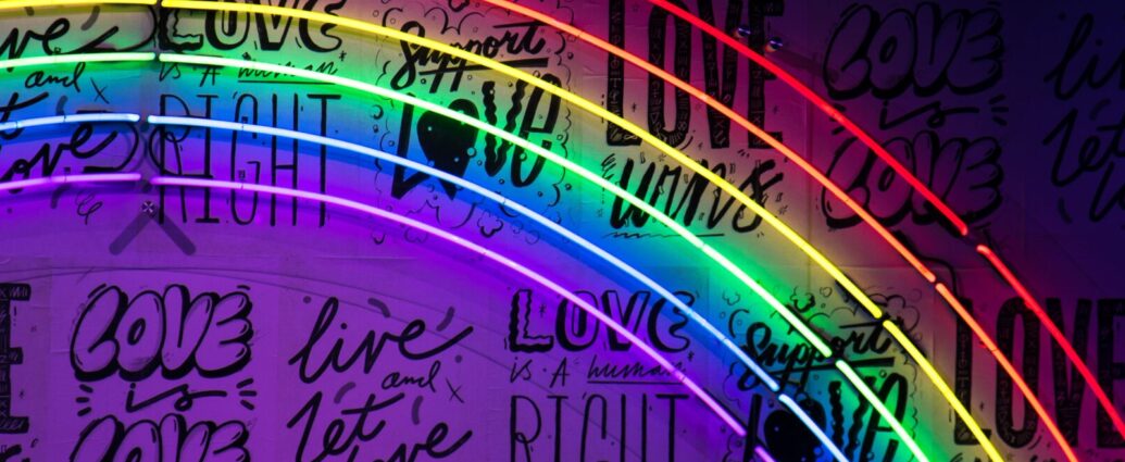 A neon pride rainbow against a darker black and purple background featuring slogans including 'love wins'. this represents the messages in songs by LGBTQ+ artists.
