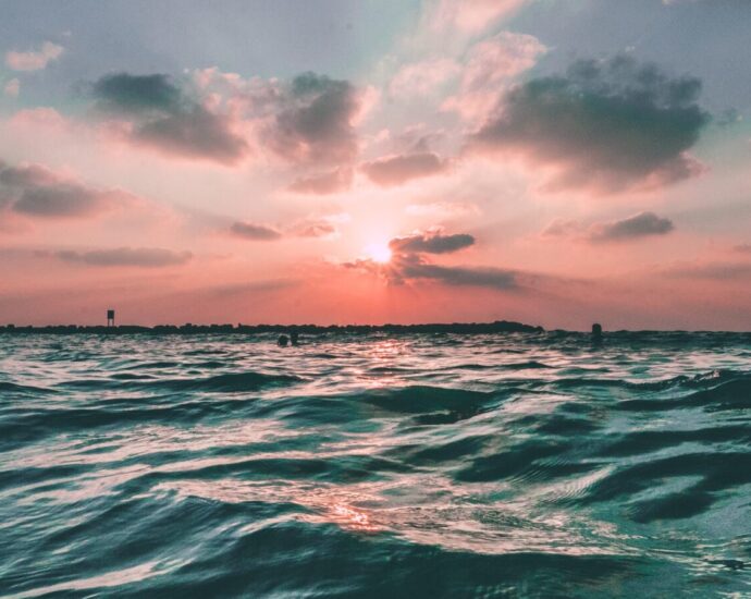 A blue ocean with calm waves underneath a candyfloss pink sunset