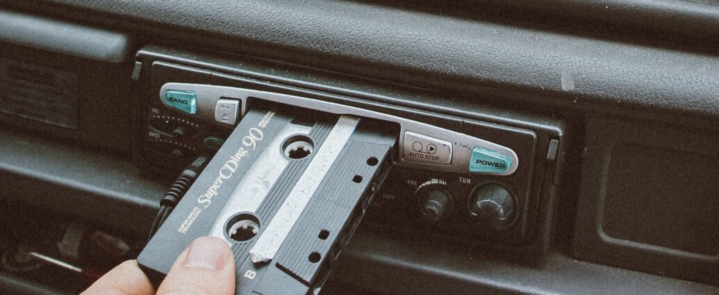 A vintage style shot of somebody inserting a cassette into the cassette player of their car.