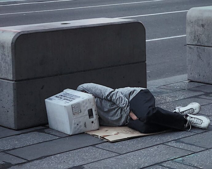 This image shows someone lying down on the floor next to what could be described as hostile architecture, because the seating area is small and has no back rest.
