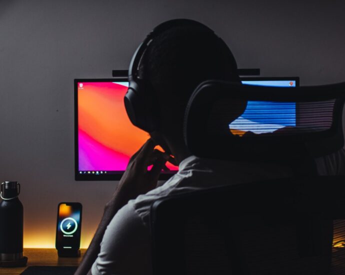 Person wears headphones in front of computer. There is a clapperboard pictured left, a common tool for YouTubers like Ballinger