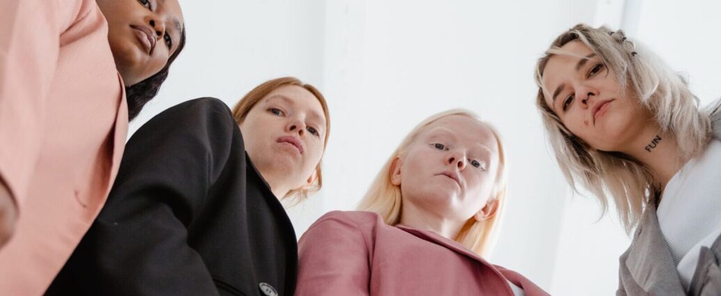 Image shows four women with stern expressions looking down towards the camera