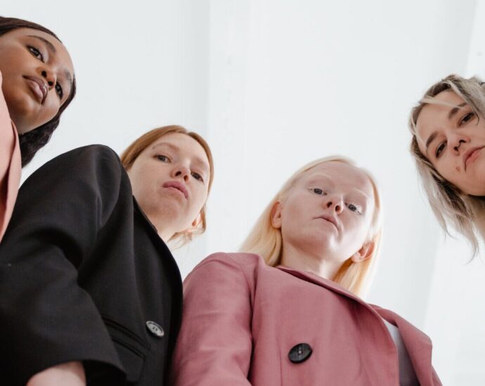 Image shows four women with stern expressions looking down towards the camera
