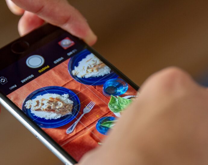 Two hands holding an iPhone, taking a picture of food.