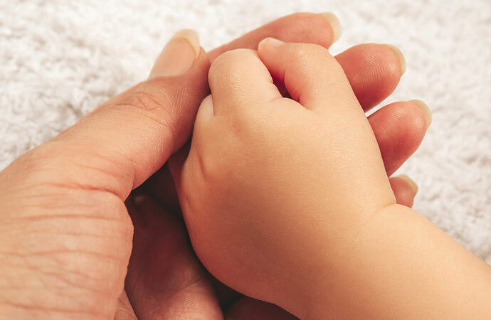 A newborn baby's hand rests on the palm of its mother.
