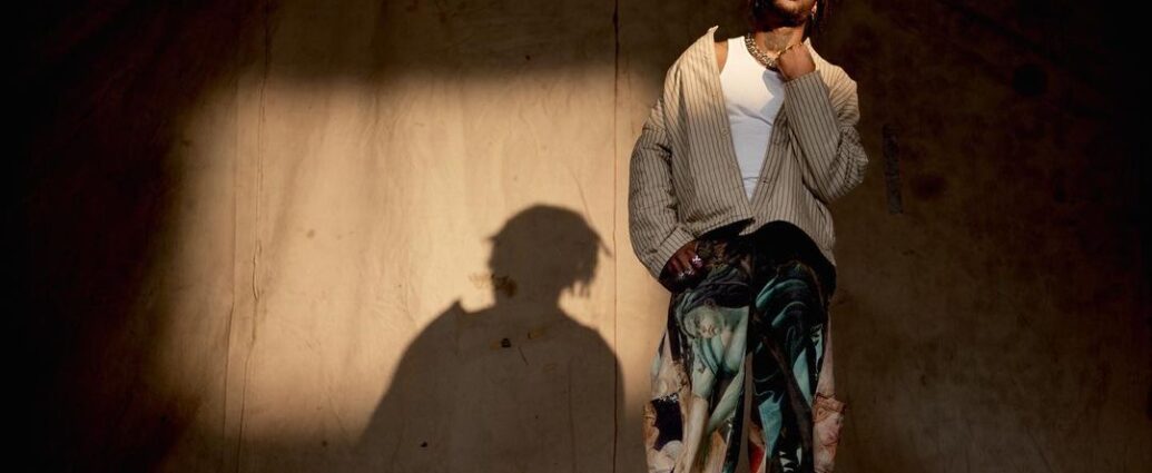 Singer VJ Jaxson stands onstage with a curtain and a shadow behind him.