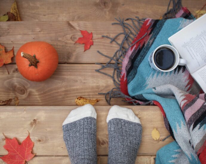 Feet in grey socks standing on stairs surrounded by autumnal leaves, a book, and a pumpkin.
