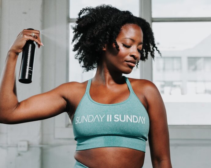 A Black woman misting her curly hair with product.