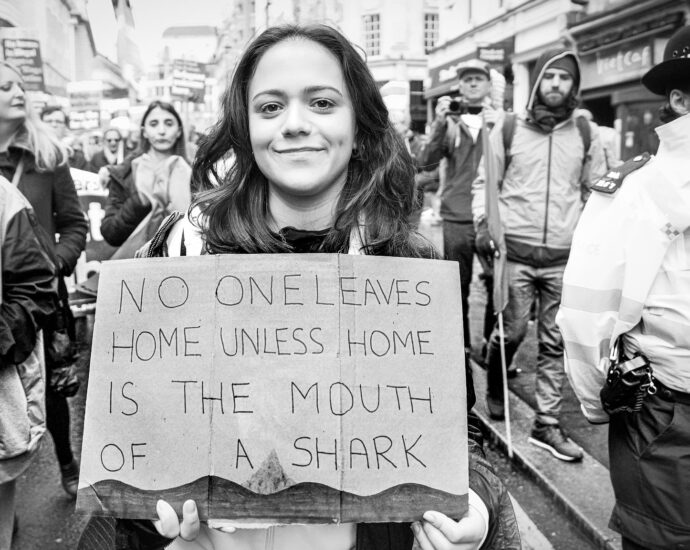 Image taken during the March Against Racism in central London on Saturday on 18 March. A protestor holds a sign reading 'No One Leaves Home Unless Home Is The Mouth Of A Shark'.