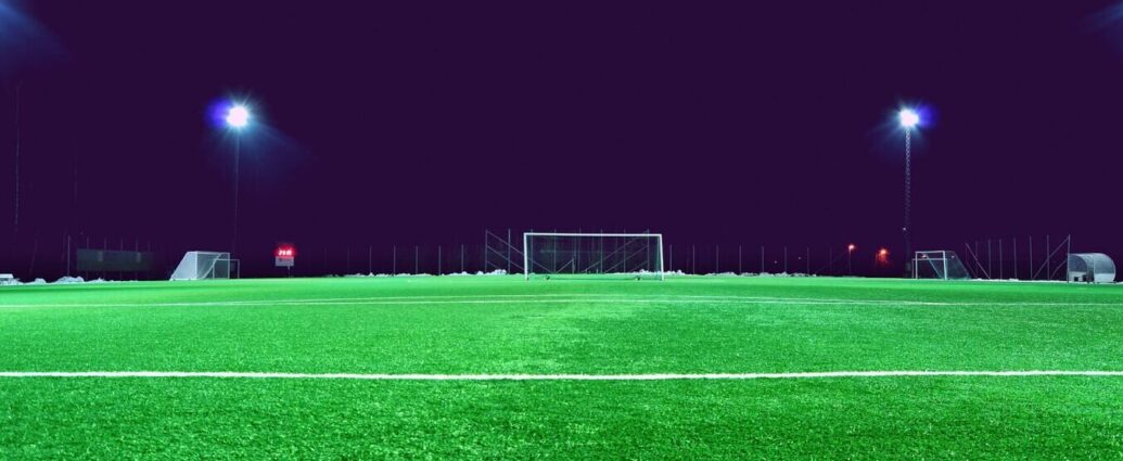 Football net and green grass of football field with dark sky lit by flood lights. Expensive Transfers.