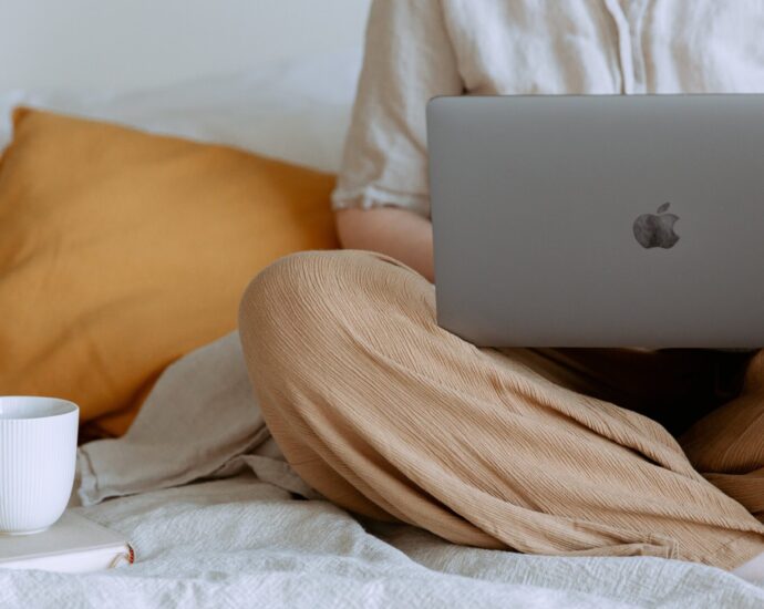 person sitting crossed legged on a bed with a laptop in their lap. My journalism journey.