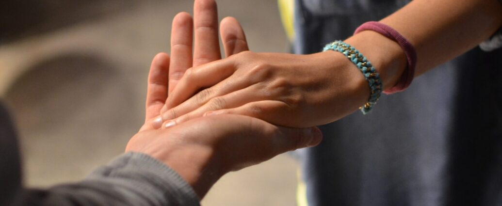 Image shows a hand reaching out to hold another hand. Help a friend with trauma.