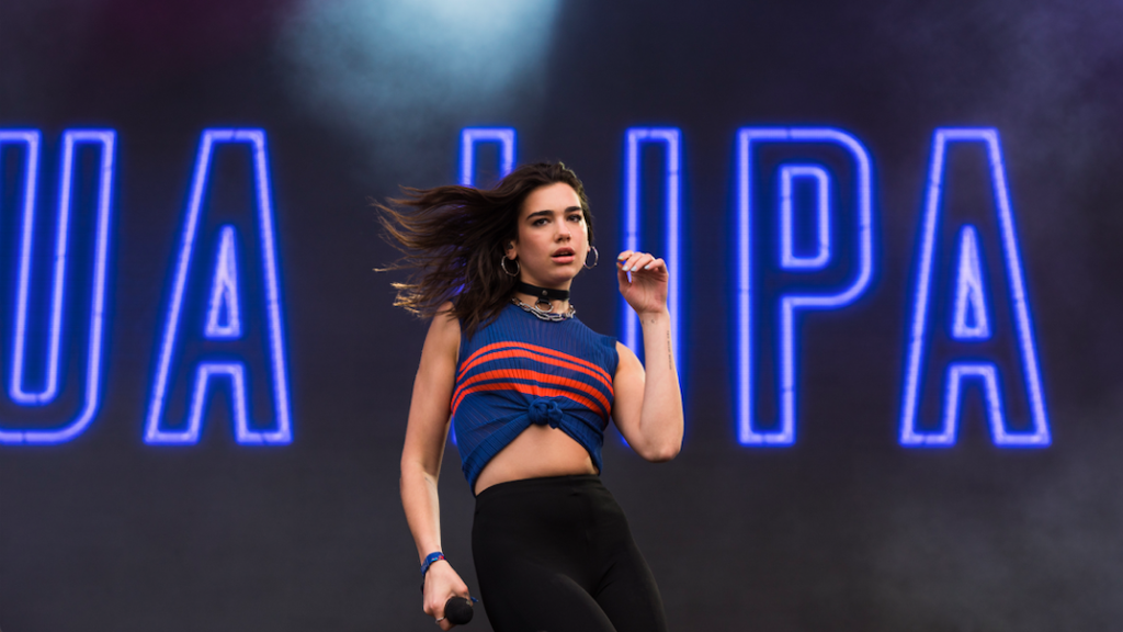 Dark haired young woman on stage back by neon lights.