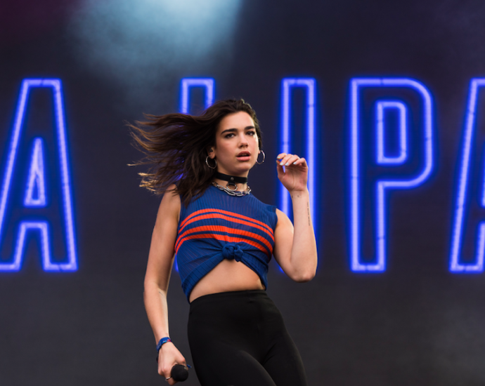 Dark haired young woman on stage back by neon lights.
