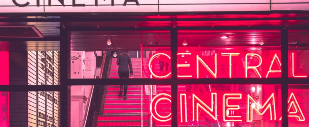 The exterior of a retro-style cinema with neon pink signs.