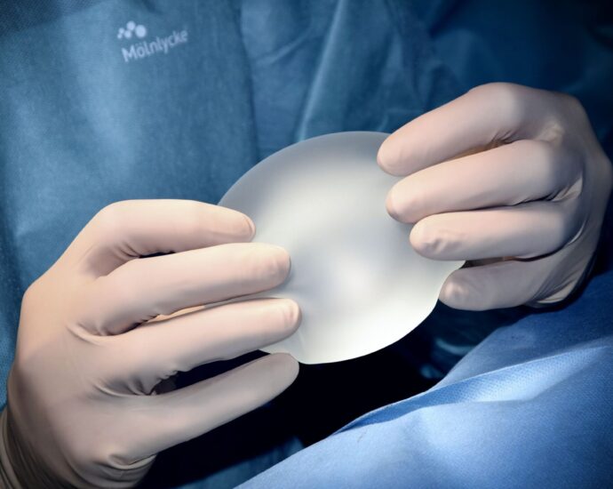 Image shows hands wearing surgical gloves holding a silicone breast implant.