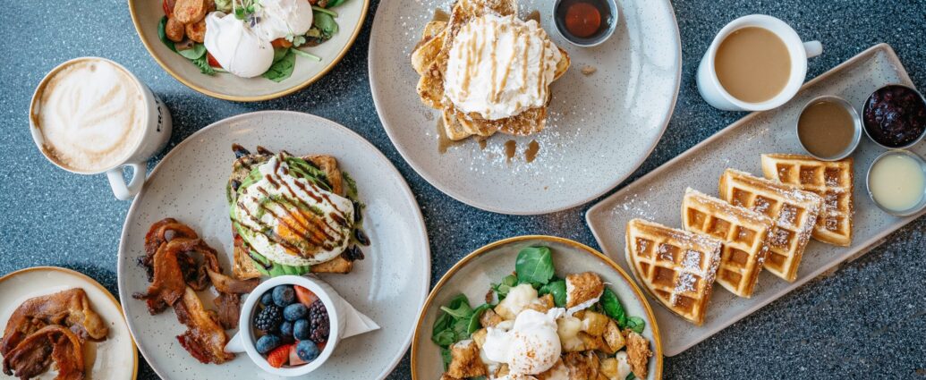 A table of brunch dishes including eggs on toast, bacon, berries and waffles.