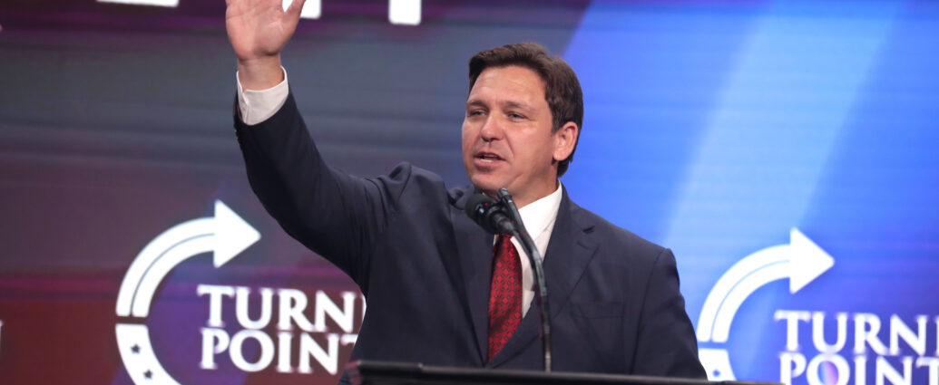 Ron DeSantis raises his arm while speaking at a podium.