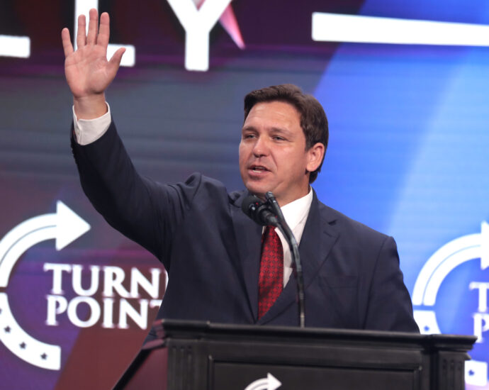 Ron DeSantis raises his arm while speaking at a podium.