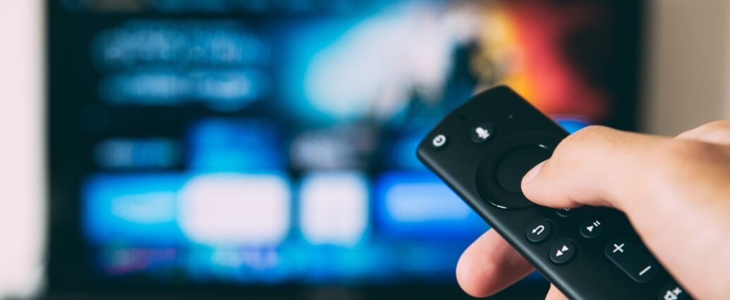 Person holding a remote control towards a blue television screen.