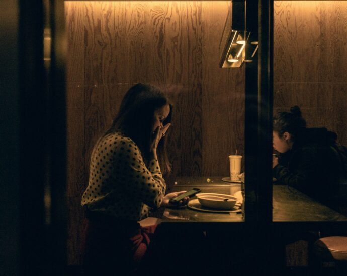 A girl sat at a restaurant table looks at her phone in shock.