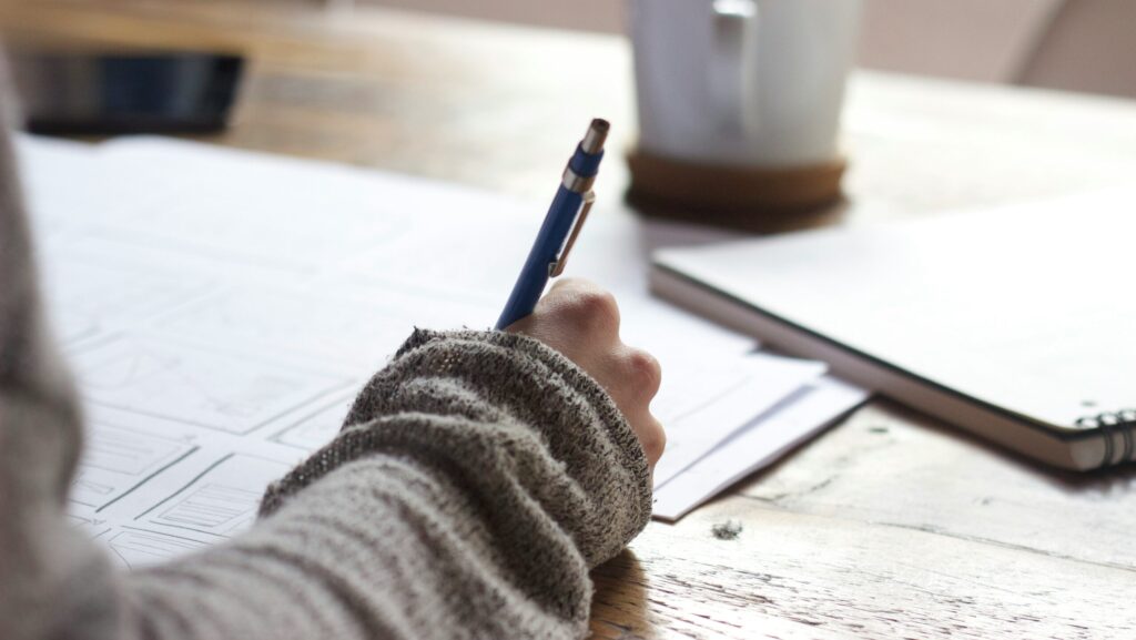 Image shows a desk with a hand writing on papers. [Finding case studies journalism]