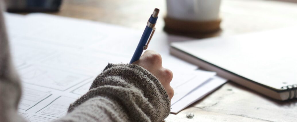 Image shows a desk with a hand writing on papers. [Finding case studies journalism]