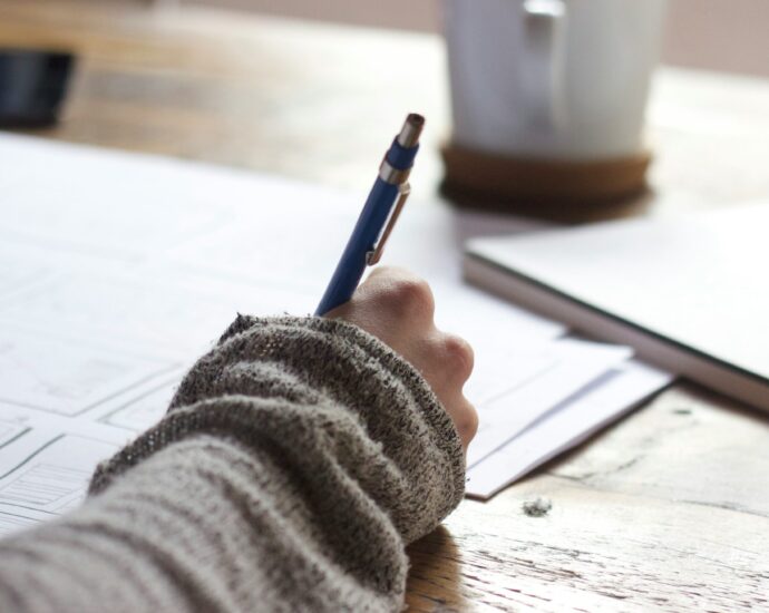 Image shows a desk with a hand writing on papers. [Finding case studies journalism]