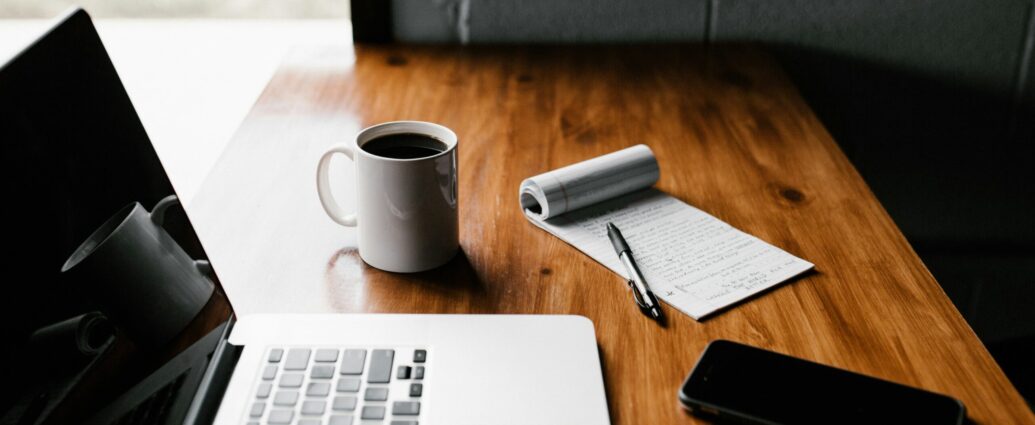 Desk with laptop, phone, coffee and notepad.