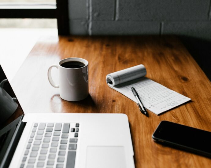 Desk with laptop, phone, coffee and notepad.