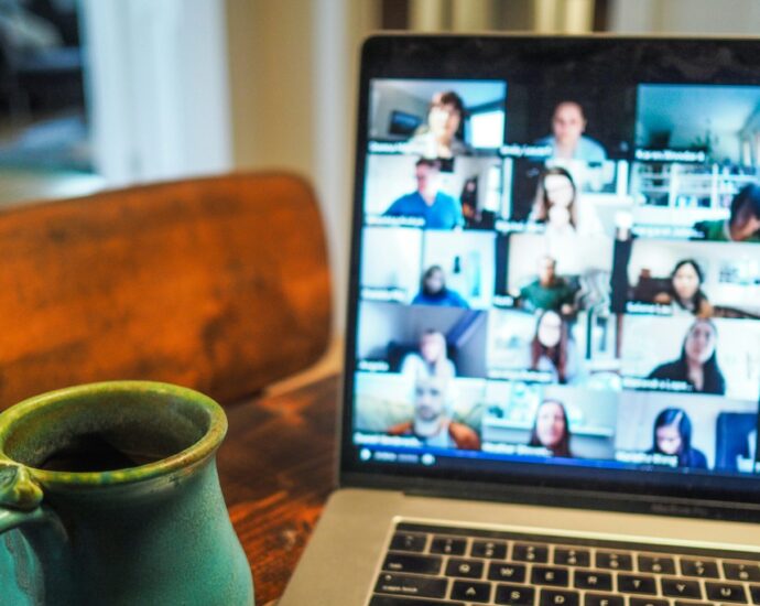 a laptop screen displaying a team video call next to a mug