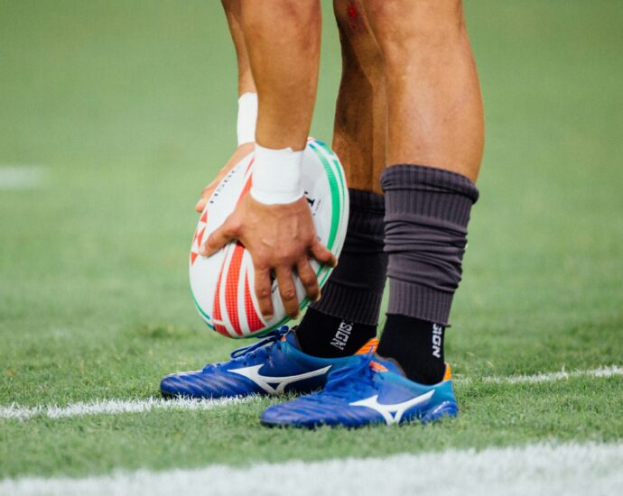 Scotland England. man wearing blue rugby boots holding rugby ball above togs.