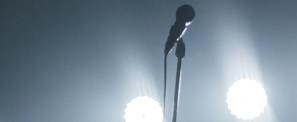 Image shows a microphone under stage lights [Touring]