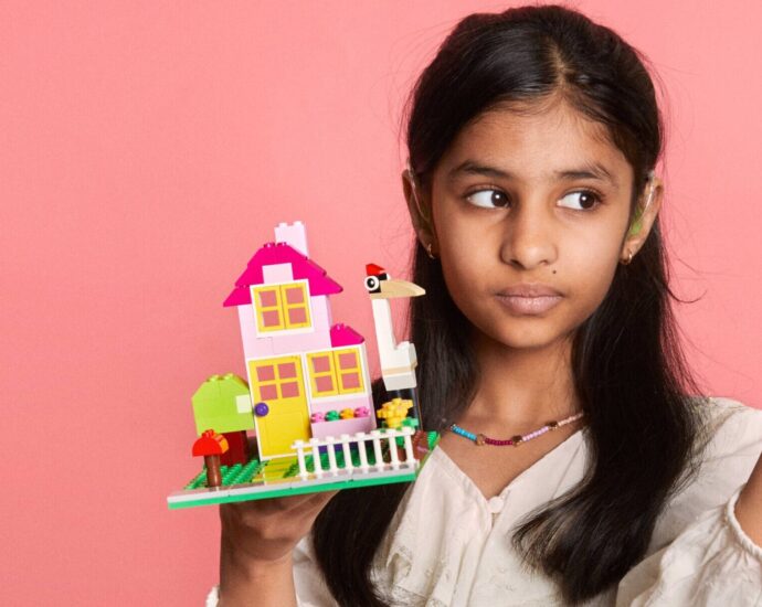 girl holding a lego house against a pink backdrop