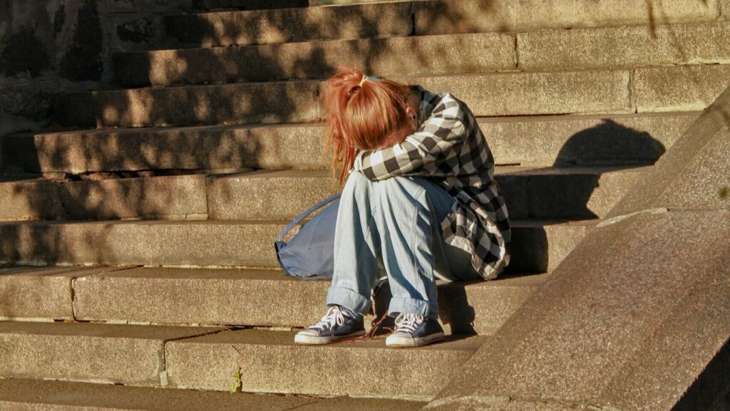 a girl sitting with her head in her lap on concrete stairs.