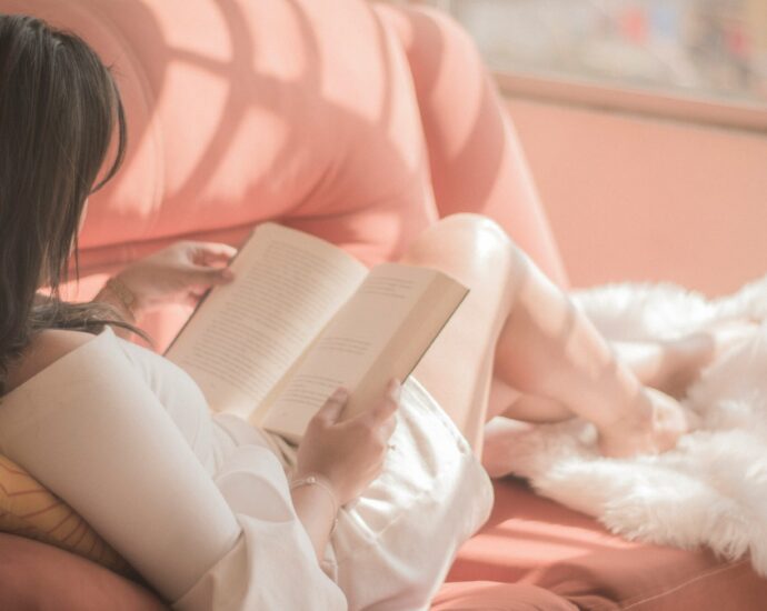 a woman reads a book on her sofa with the sun streaming through the window.