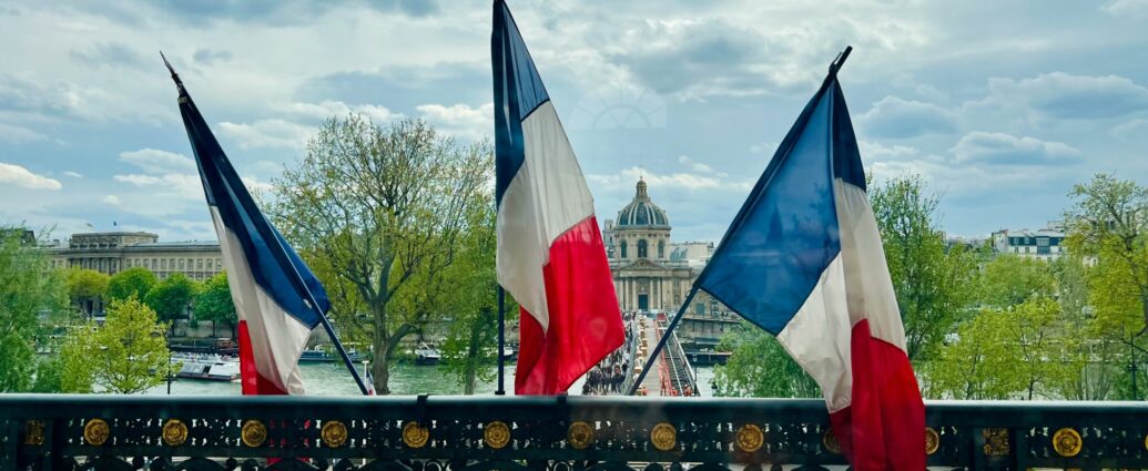 Three french flags sit upright from a balcony overlooking Paris.
