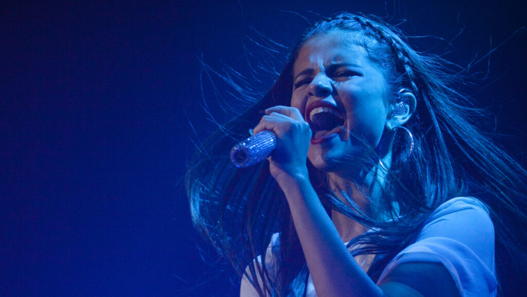 Selena Gomez singing with emotion into a microphone.