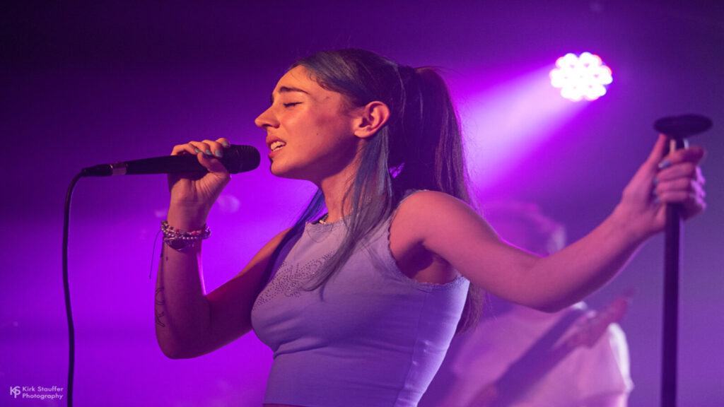 Samia singing in to a microphone with purple lighting in the background