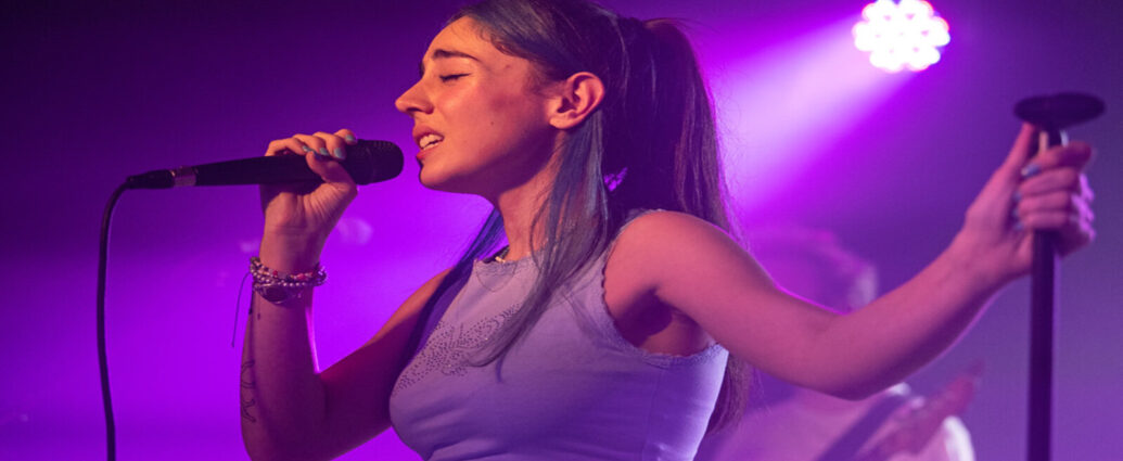 Samia singing in to a microphone with purple lighting in the background