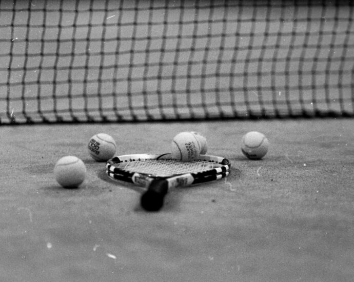Black and white picture of a tennis racket lying on the ground surrounded by tennis balls.