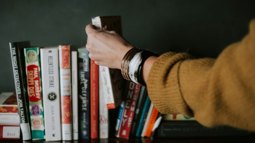 Person picking books from bookshelf