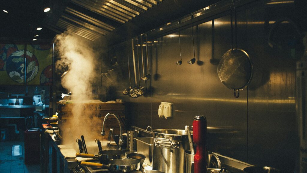 An industrial kitchen with large pots cooking on the stove.