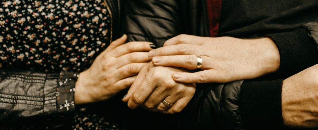 A man and woman holding hands, wearing wedding rings.